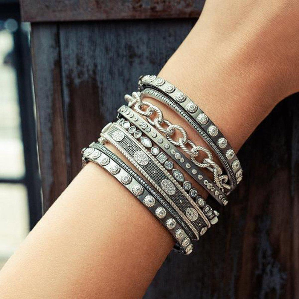 Stack of silver and dark gray bangles adorned with sparkling stones on a wrist.
