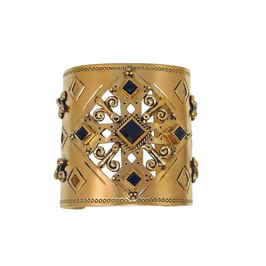 Gold cuff bracelet with ornate cutout design and dark stones.
