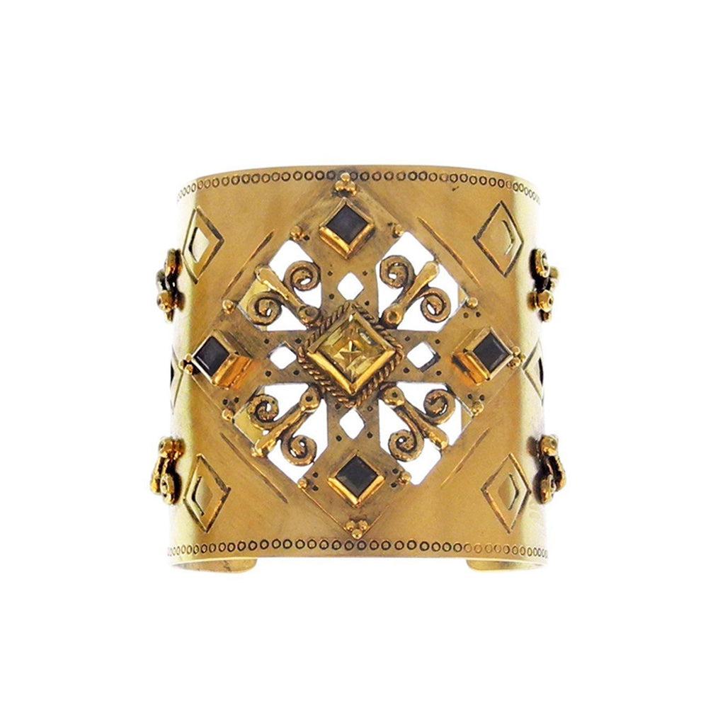 Gold cuff bracelet with ornate detailing and dark gemstone accents.

