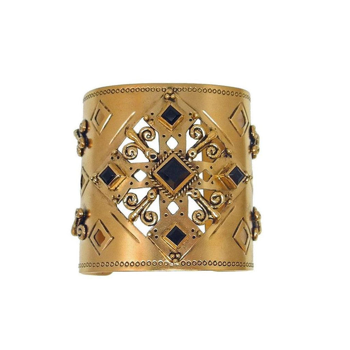 Gold cuff bracelet with ornate cutout design and dark stones.
