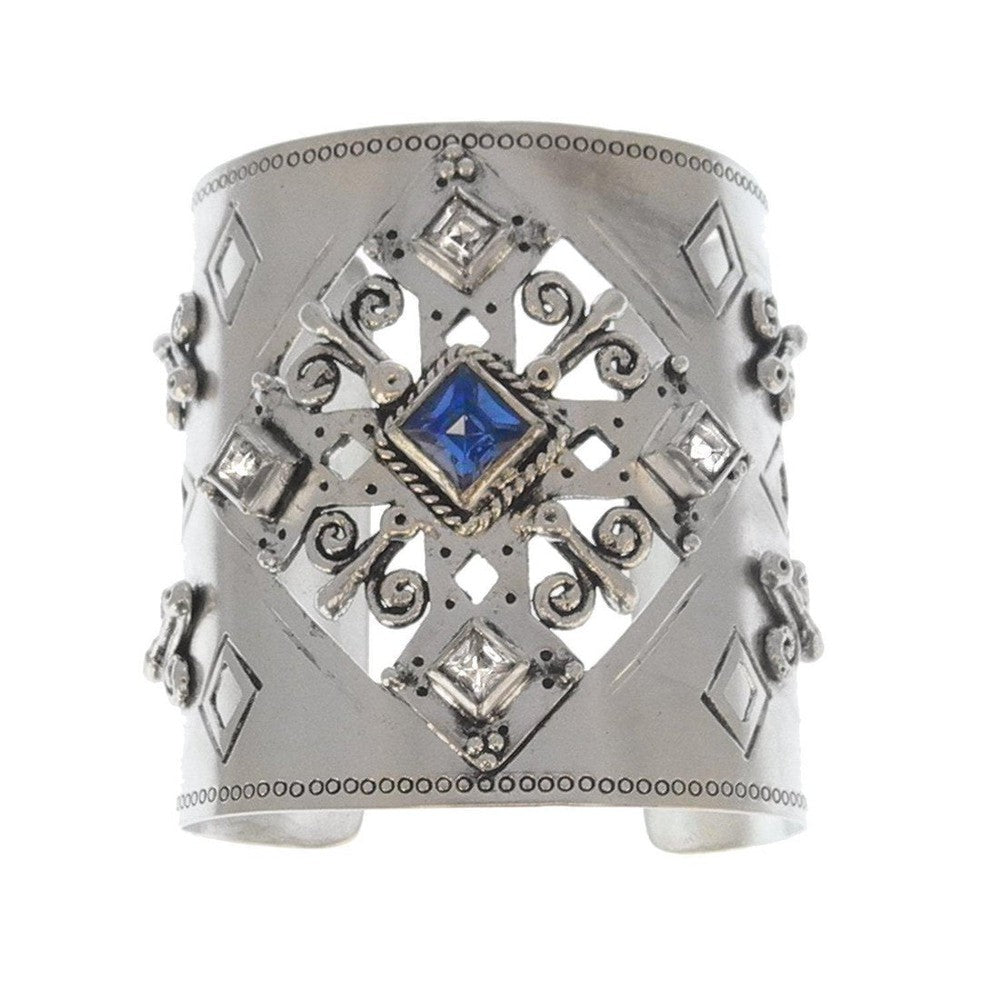 Silver cuff bracelet featuring an ornate design, blue sapphire, and clear stones.
