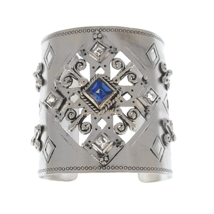Silver cuff bracelet featuring an ornate design, blue sapphire, and clear stones.
