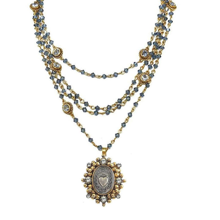 Layered gold necklace with blue beads and ornate silver pendant featuring a heart motif.
