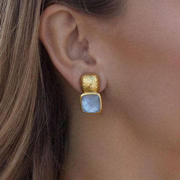 Gold and light blue gemstone clip earrings on model's ear.
