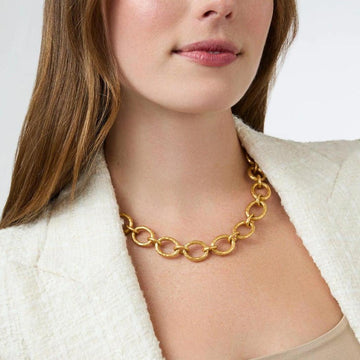 Gold hammered-metal link necklace on model wearing cream jacket.
