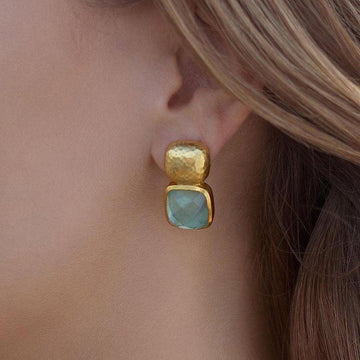Gold hammered-metal and light-blue gemstone earrings worn on model's ear.
