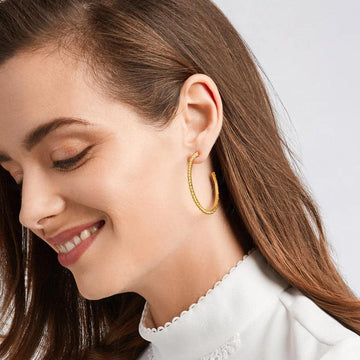 Gold textured hoop earrings on a woman's ear.
