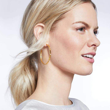 Gold hoop earrings with small accents, worn by a woman with blonde hair.
